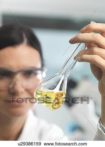 Stock Photo - Chemist looking at solution in flask during research experiment. Fotosearch