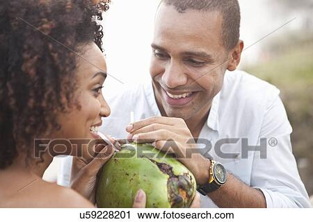 Stock Image - "Close up of couple sharing coconut milk at beach, Rio De Janeiro, Brazil". Fotosearch