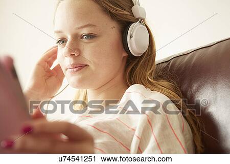 Stock Image - Close up of girl on sofa listening to music on headphones. Fotosearch