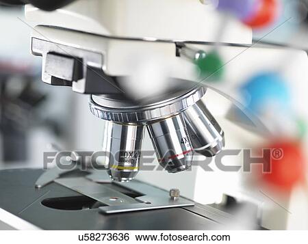 Stock Photograph - Close up of microscope viewing sample with a ball and stick molecular model illustrating ground breaking research. Fotosearch