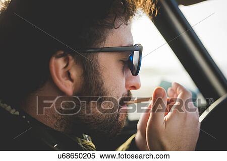 Stock Photography - Close up of mid adult man in car lighting a cigarette. Fotosearch