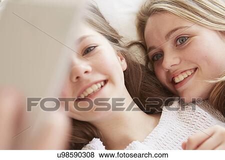 Stock Photo - Close up of two girls lying on bed taking smartphone selfie. Fotosearch