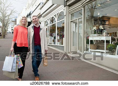 Stock Photo - Couple carrying shopping bags on village street. Fotosearch