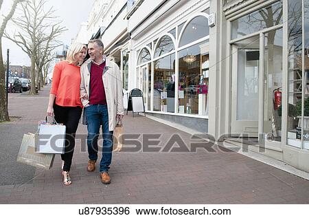 Couple carrying shopping on village street View Large Photo Image Stock Photograph - Couple carrying shopping on village street. Fotosearch