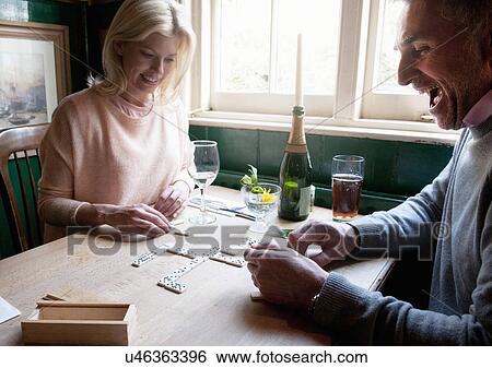 Stock Photograph - Couple drinking and playing dominoes in pub. Fotosearch