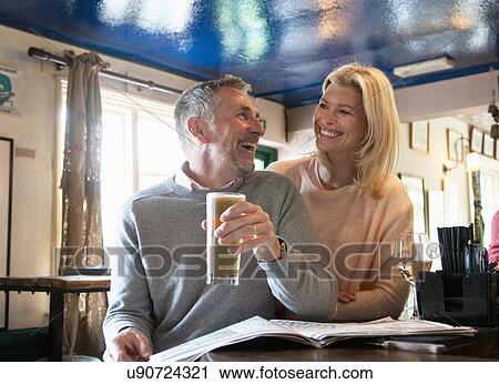 Stock Image - Couple laughing and reading newspaper in pub. Fotosearch