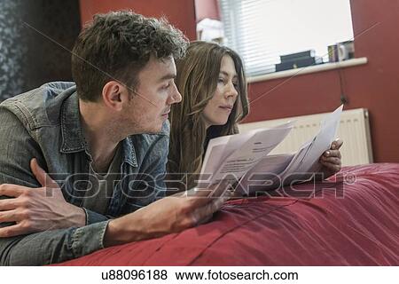 Stock Photo - Couple lying on bed looking at paperwork. Fotosearch