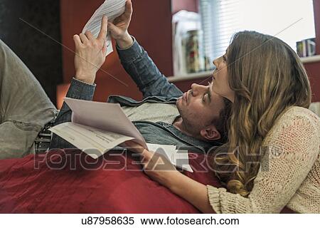 Couple lying on bed reading paperwork View Large Photo Image Stock Photography - Couple lying on bed reading paperwork. Fotosearch