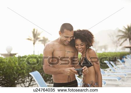 Stock Photography - "Couple reviewing photographs on digital camera at hotel poolside, Rio De Janeiro, Brazil". Fotosearch