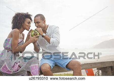 Stock Image - "Couple sharing coconut milk at beach, Rio De Janeiro, Brazil". Fotosearch