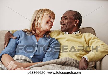 Stock Image - "Couple sitting on sofa, smiling". Fotosearch