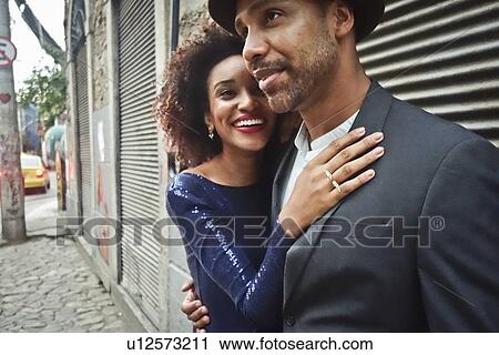 Stock Image - "Couple standing together in urban environment, hugging, smiling". Fotosearch