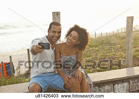 Stock Image - "Couple taking smartphone selfie at beach, Rio De Janeiro, Brazil". Fotosearch