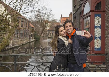 Stock Photo - "Couple taking smartphone selfie, Bruges, Flanders, Belgium". Fotosearch
