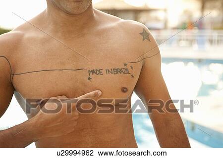 Stock Image - "Cropped shot of man pointing to chest tattoo at hotel swimming pool, Rio De Janeiro, Brazil". Fotosearch