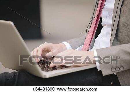 Cropped shot of young city businessman sitting on sidewalk typing on laptop View Large Photo Image Stock Image - Cropped shot of young city businessman sitting on sidewalk typing on laptop. Fotosearch