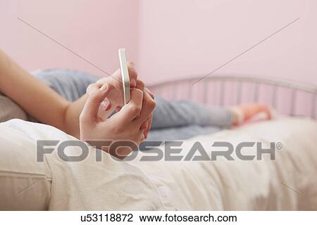 Cropped view of girl lying on bed reading smartphone text message View Large Photo Image Stock Image - Cropped view of girl lying on bed reading smartphone text message. Fotosearch