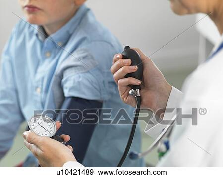 Stock Photo - Doctor reading blood pressure of young boy in clinic. Fotosearch