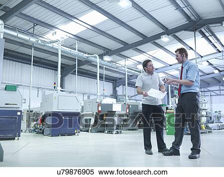 Stock Photography - Engineer and apprentice discussing drawings in factory. Fotosearch