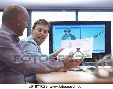 Stock Photo - Engineer and client inspecting automotive part at desk. Fotosearch