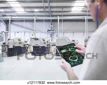 Stock Image - "Engineer using digital tablet by production line in factory, close up". Fotosearch