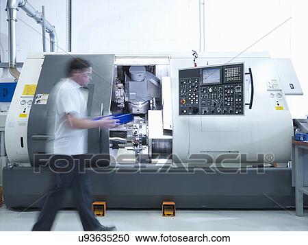 Stock Image - Engineer working with CNC lathe in factory. Fotosearch