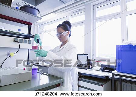 Picture - Female scientist pipetting sample into volumetric flask. Fotosearch