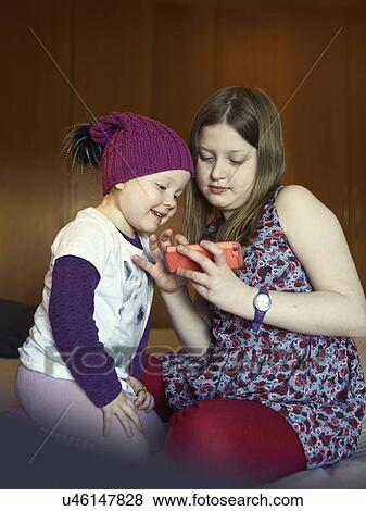 Stock Photo - Female toddler and sister using touchscreen on smartphone. Fotosearch