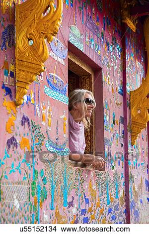Picture - "Female tourist looking out of Wat Xieng Thong window, Luang Prabang, Laos". Fotosearch