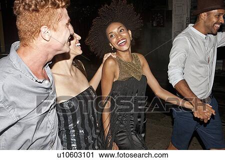 Stock Image - Four friends walking along street together at night. Fotosearch