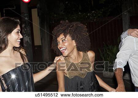 Stock Image - Four friends walking along street together at night. Fotosearch
