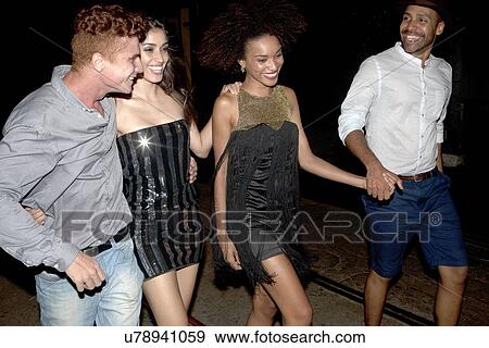 Four friends walking along street together at night View Large Photo Image Stock Photo - Four friends walking along street together at night. Fotosearch