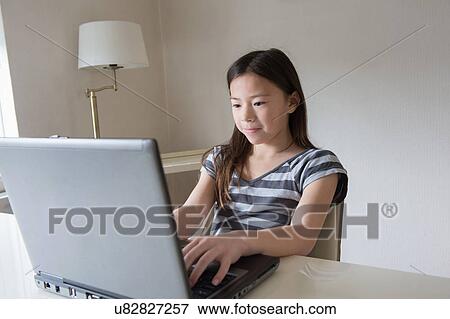 Girl at table typing on laptop View Large Photo Image Stock Photo - Girl at table typing on laptop. Fotosearch