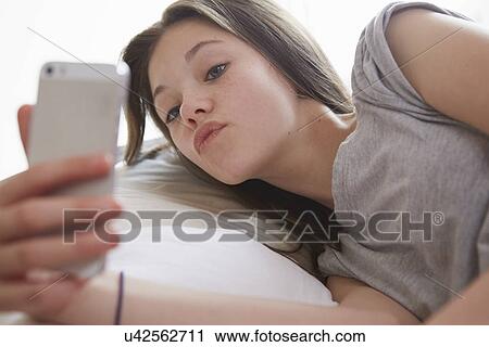 Girl lying on bed peering at smartphone text message View Large Photo Image Stock Image - Girl lying on bed peering at smartphone text message. Fotosearch