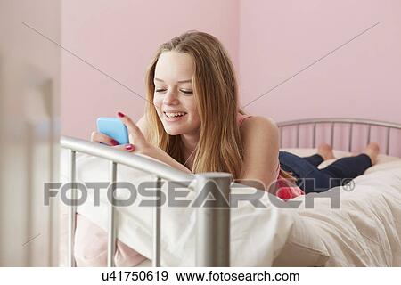 Girl lying on bed reading text message on smartphone View Large Photo Image Stock Photo - Girl lying on bed reading text message on smartphone. Fotosearch