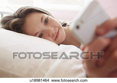 Girl lying on bed texting on smartphone View Large Photo Image Picture - Girl lying on bed texting on smartphone. Fotosearch