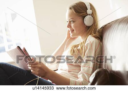 Girl on sofa wearing headphones listening to music from digital tablet View Large Photo Image Stock Image - Girl on sofa wearing headphones listening to music from digital tablet. Fotosearch