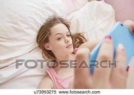 Stock Photography - Girl posing on bed for smartphone selfie. Fotosearch