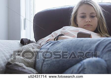 Picture - Girls reading smartphone texts on sofa. Fotosearch