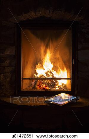 Stock Image - Glowing log fire and digital tablet on hearth. Fotosearch