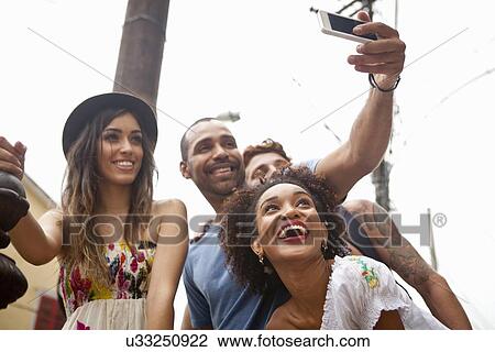 Stock Image - "Group of friends taking self portrait, using smartphone". Fotosearch