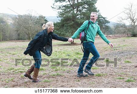 Hiking couple holding hands and running in field View Large Photo Image Stock Photo - Hiking couple holding hands and running in field. Fotosearch