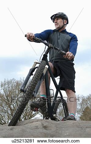 Low angle view of mature male mountain biker looking out from rock formation View Large Photo Image Stock Image - Low angle view of mature male mountain biker looking out from rock formation. Fotosearch