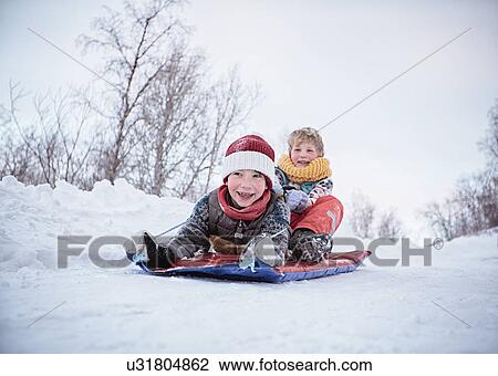 Stock Image - "Low angle view of two brothers on toboggan on snow covered hill, Hemavan, Sweden". Fotosearch