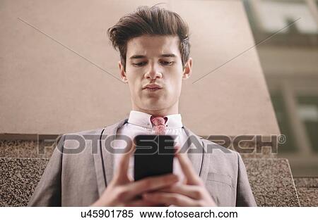 Low angle view of young city businessman reading smartphone text View Large Photo Image Stock Photography - Low angle view of young city businessman reading smartphone text. Fotosearch
