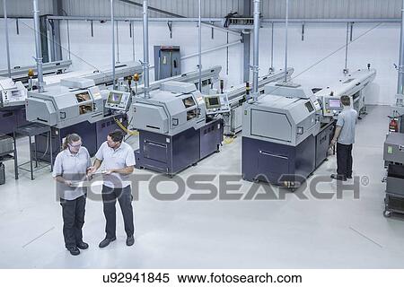 Stock Photography - Male and female engineers discussing manufactured parts. Fotosearch
