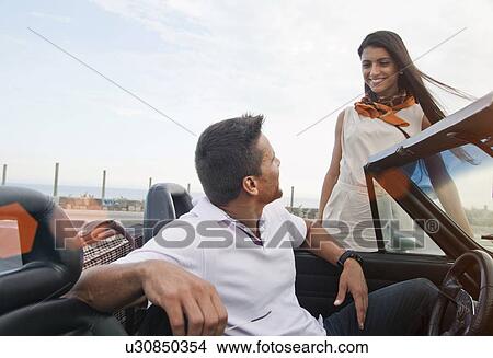Picture - "Man in convertible car, woman standing beside car, smiling". Fotosearch