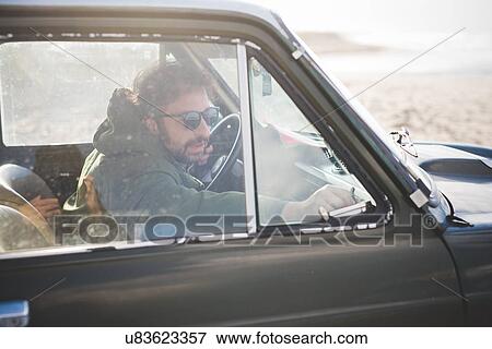 Stock Photo - Man in parked vintage car lat beach fastening window. Fotosearch