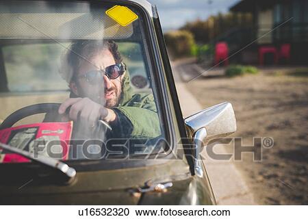 Man in parked vintage car looking through wing mirror View Large Photo Image Stock Image - Man in parked vintage car looking through wing mirror. Fotosearch