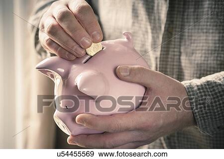 Stock Photo - Man inserting coin into piggy bank. Fotosearch